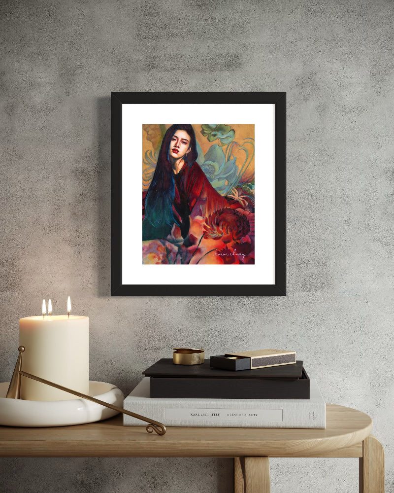 Framed artwork of a woman with flowers on a wall above a table with books and a candle.