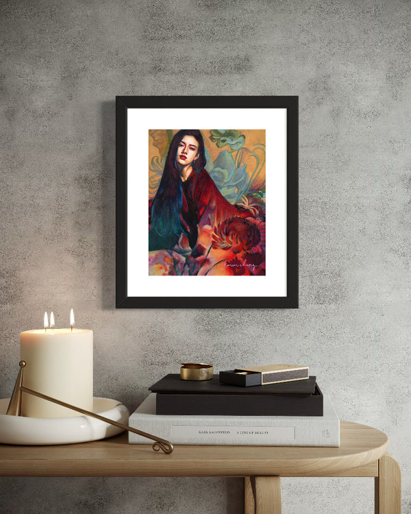 Framed artwork of a woman with flowers on a wall above a table with books and a candle.