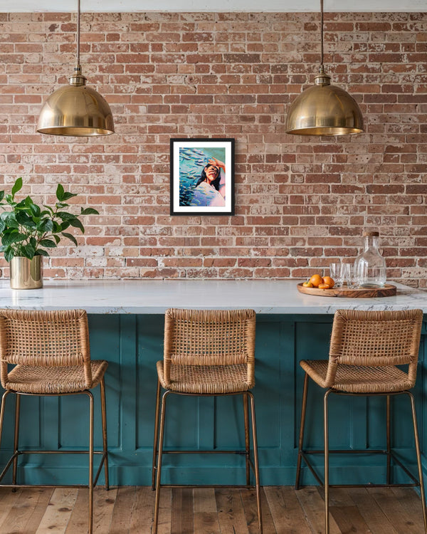 Kitchen bar with teal cabinets, marble countertop, wicker chairs, and a brick wall with framed artwork.