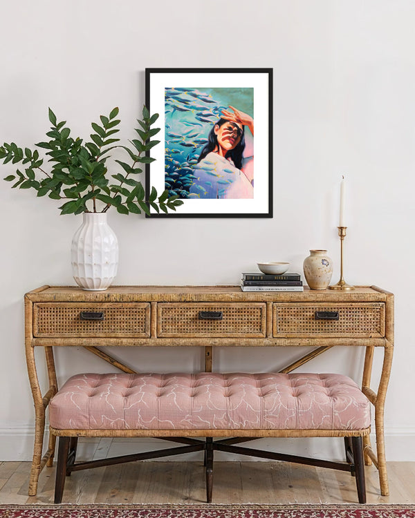 Framed artwork above a wooden console table with a pink bench.