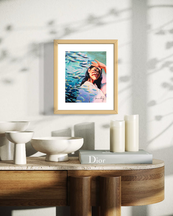 Framed artwork of a woman underwater on a table with decor items.