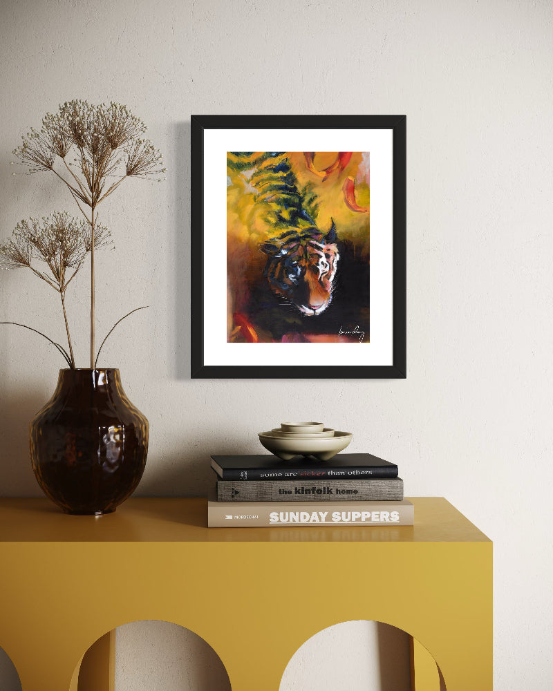 Framed artwork of a tiger on a wall above a yellow table with books and a vase.