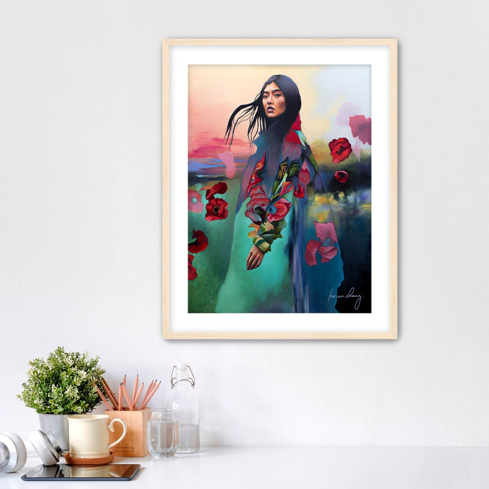 Framed artwork of a woman with flowers on a white wall above a desk.