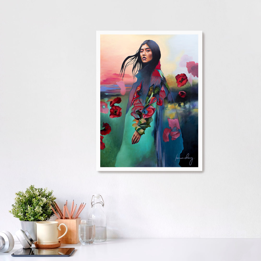 Framed artwork of a woman with flowers on a white wall above a desk.