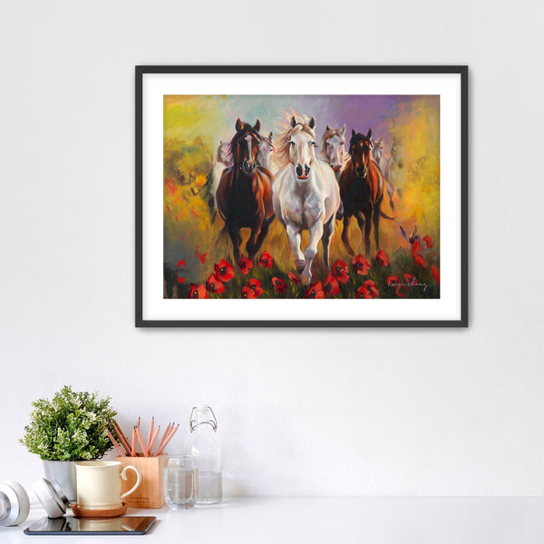 Framed painting of horses running with flowers on a wall above a desk.