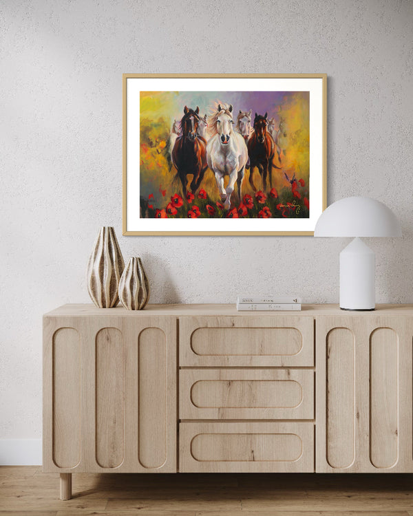 Framed painting of horses running with flowers on a wall above a wooden cabinet.