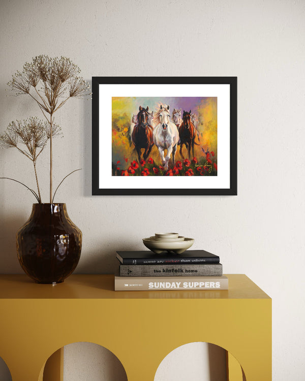 Framed artwork of horses on a wall above a yellow console table with books and a vase.