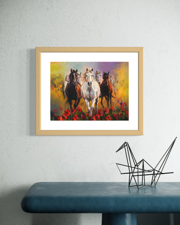Framed artwork of horses running through flowers on a wall above a blue table with a black decorative object.